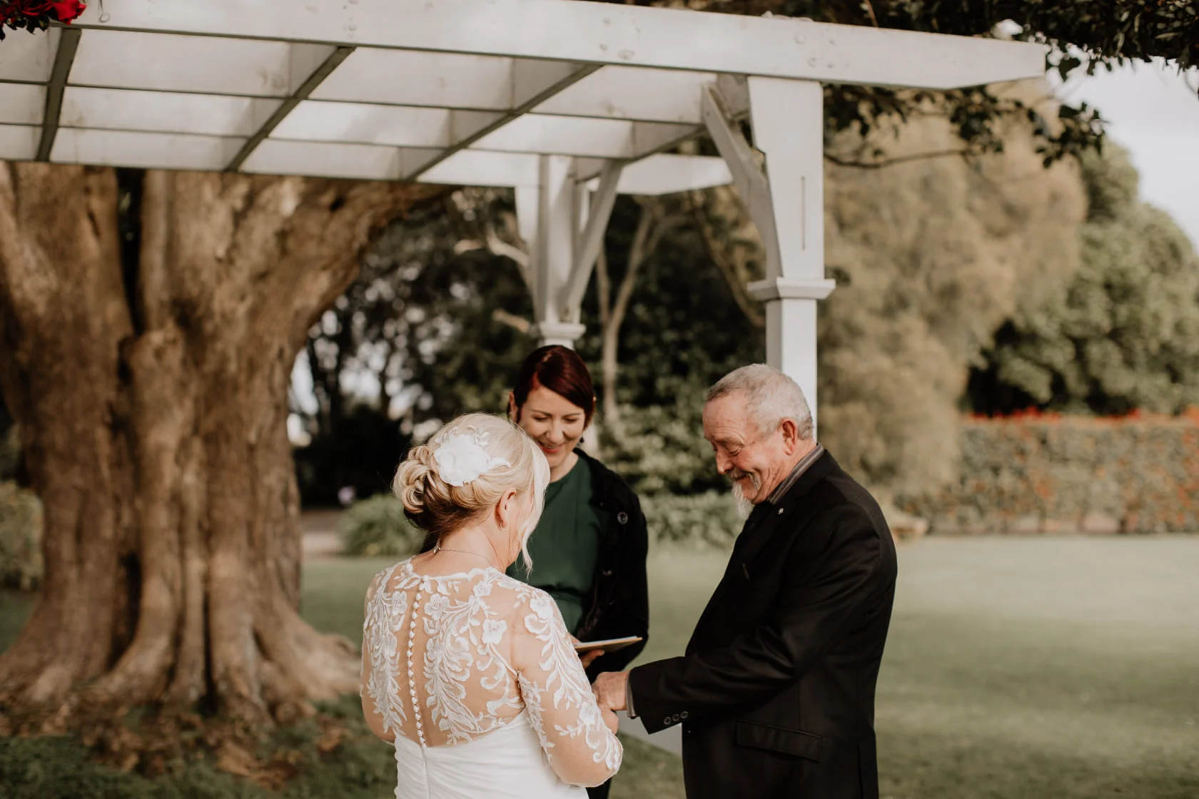 A couple during their bespoke wedding ceremony in a Canterbury garden, golden afternoon light filtering through the trees